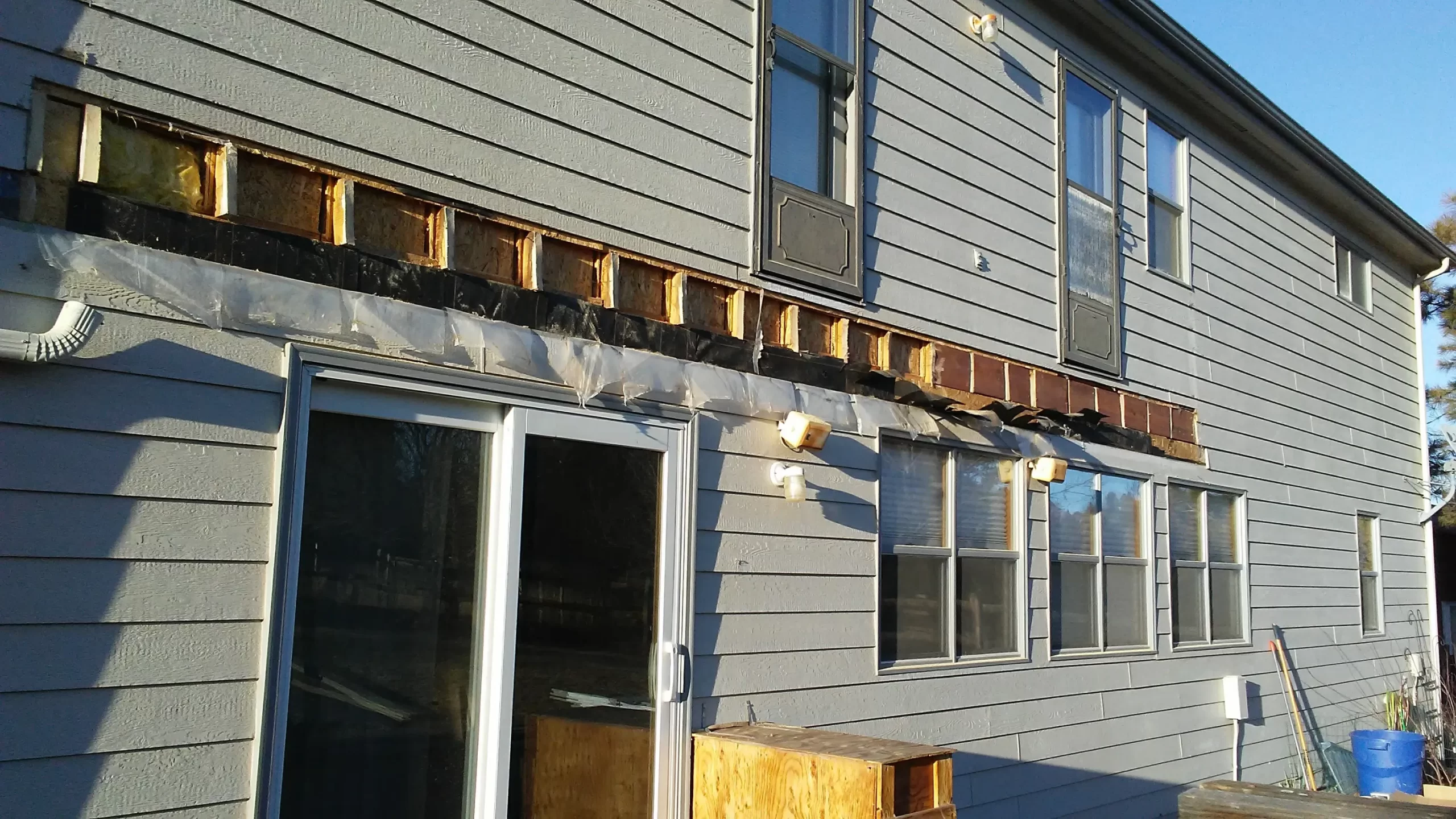 gallery (10) A gray two-story house with exposed beams above several windows and a sliding glass door.