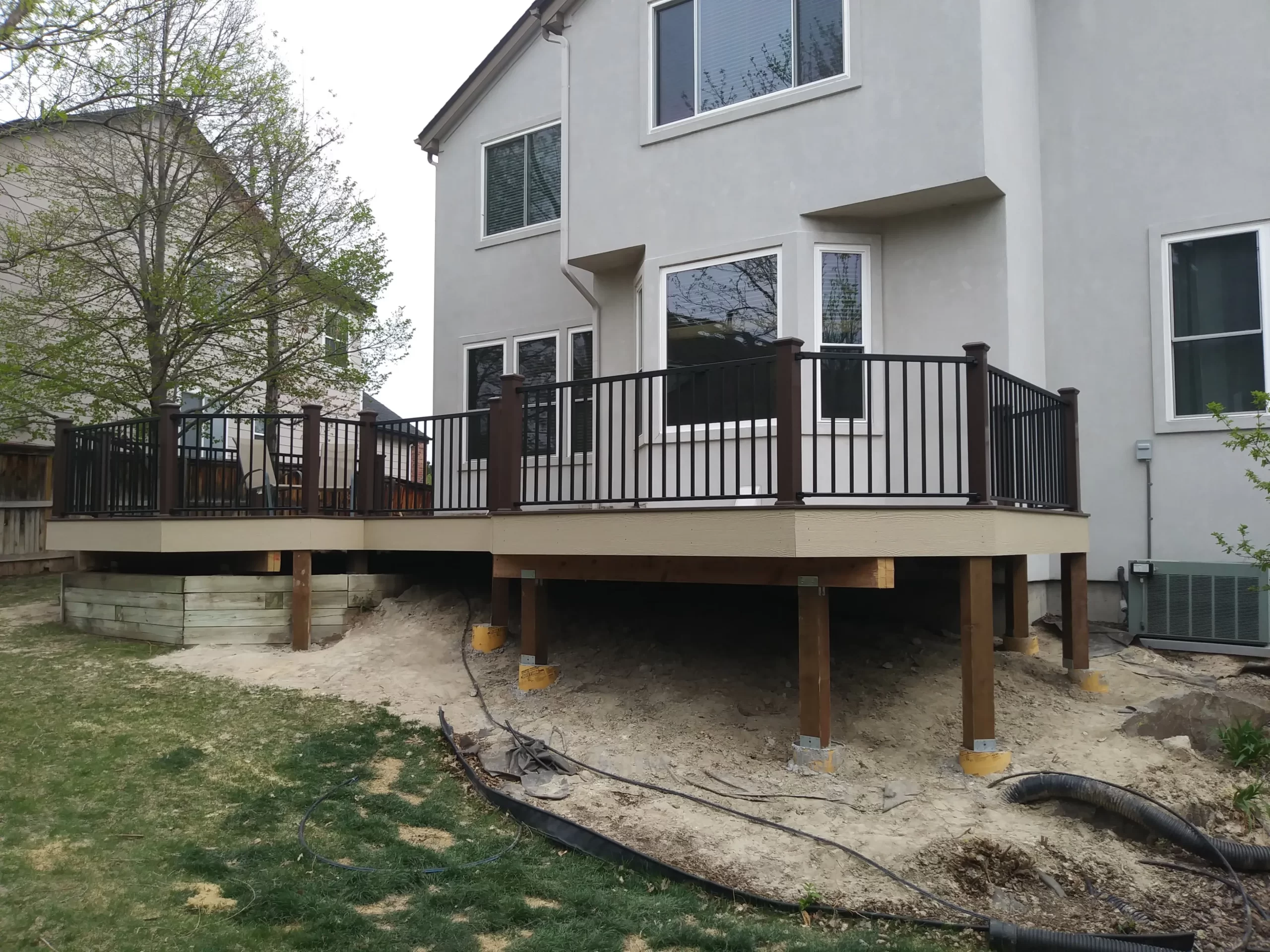 gallery (13) Elevated wooden deck with black railing attached to a two-story house in a backyard setting.