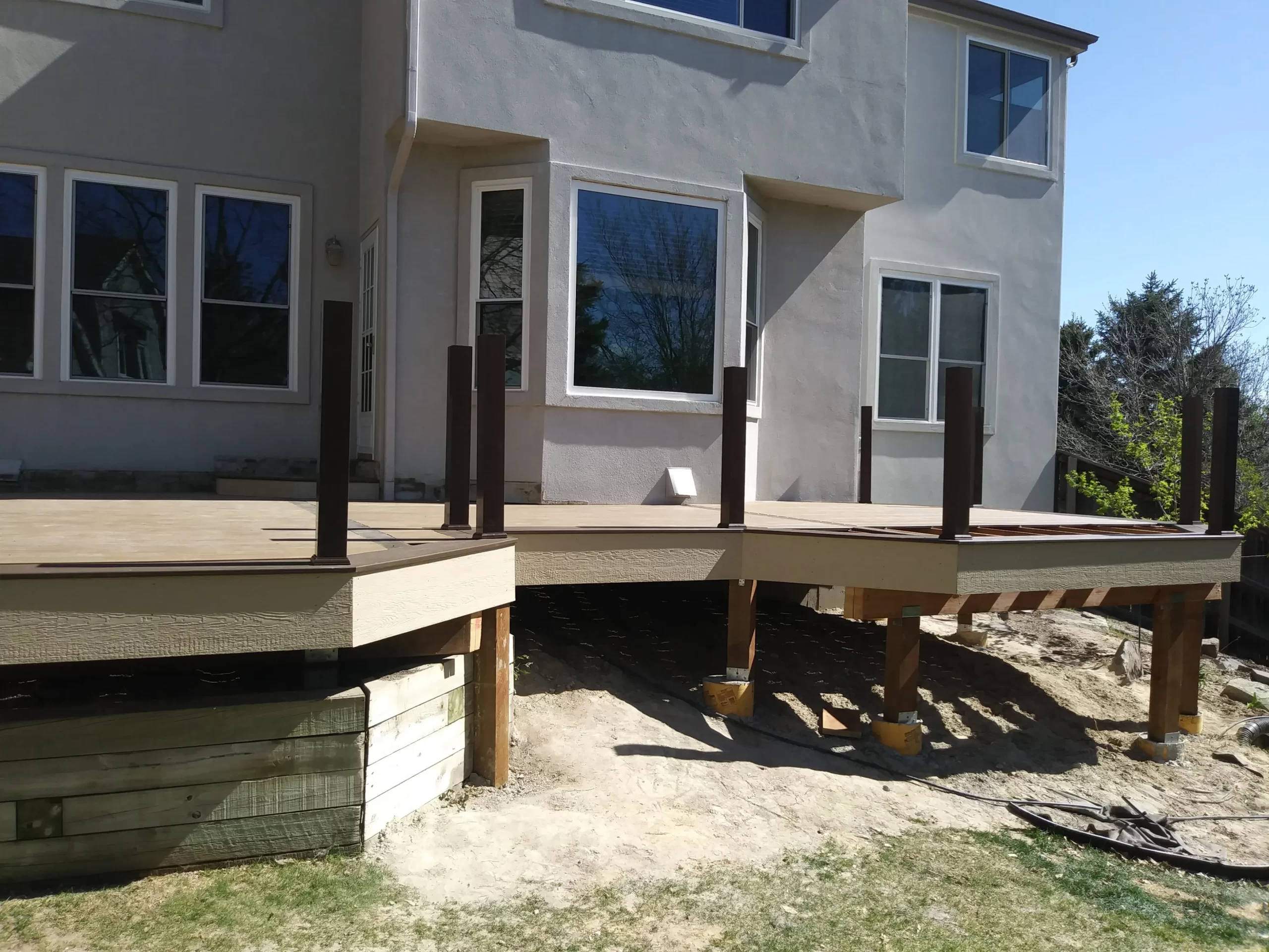 gallery (14) Unfinished wooden deck attached to a beige house, with support beams and no railing.