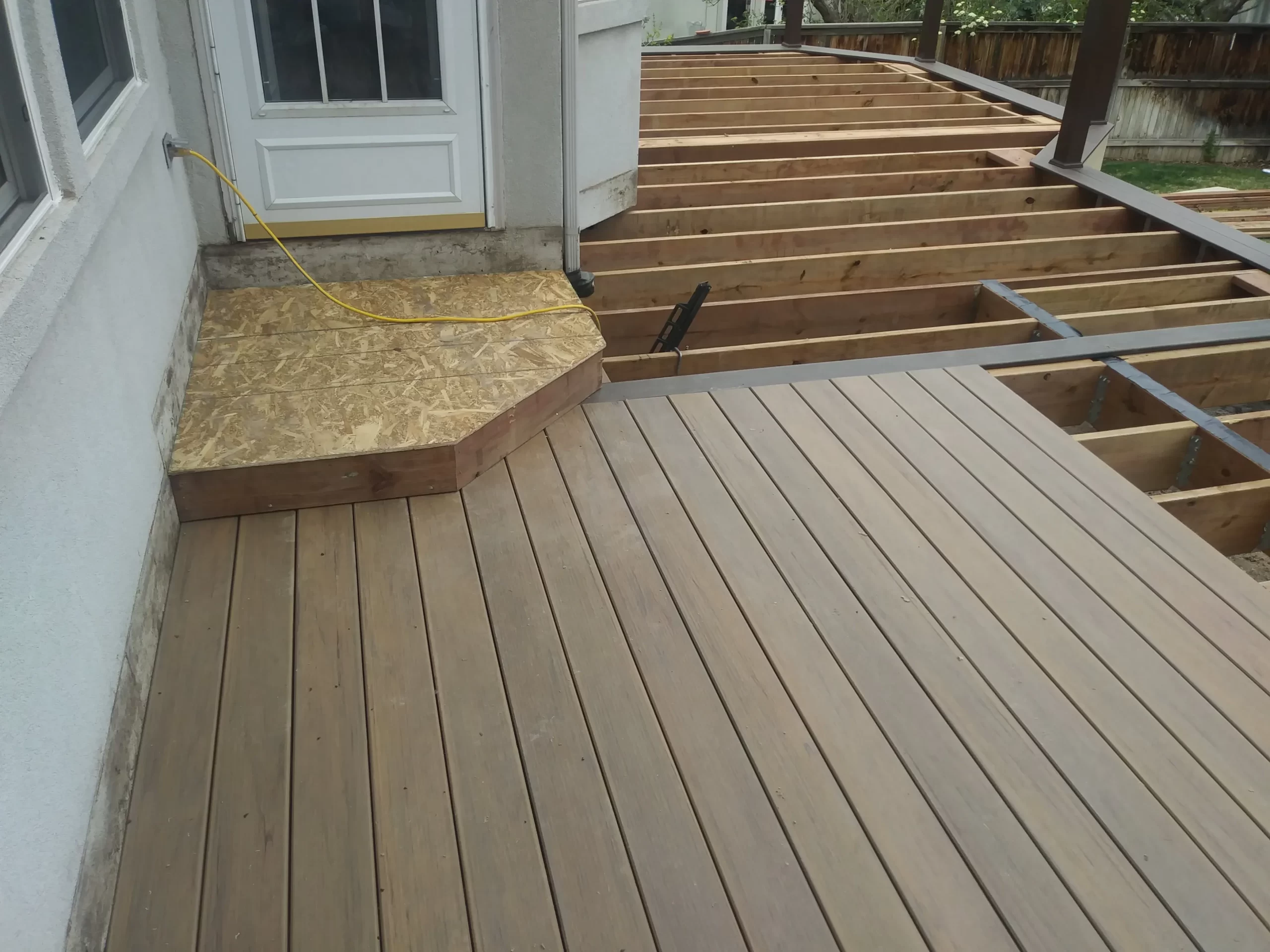 gallery (15) Wooden deck under construction, with partially completed boards and visible joists, near a white exterior door.