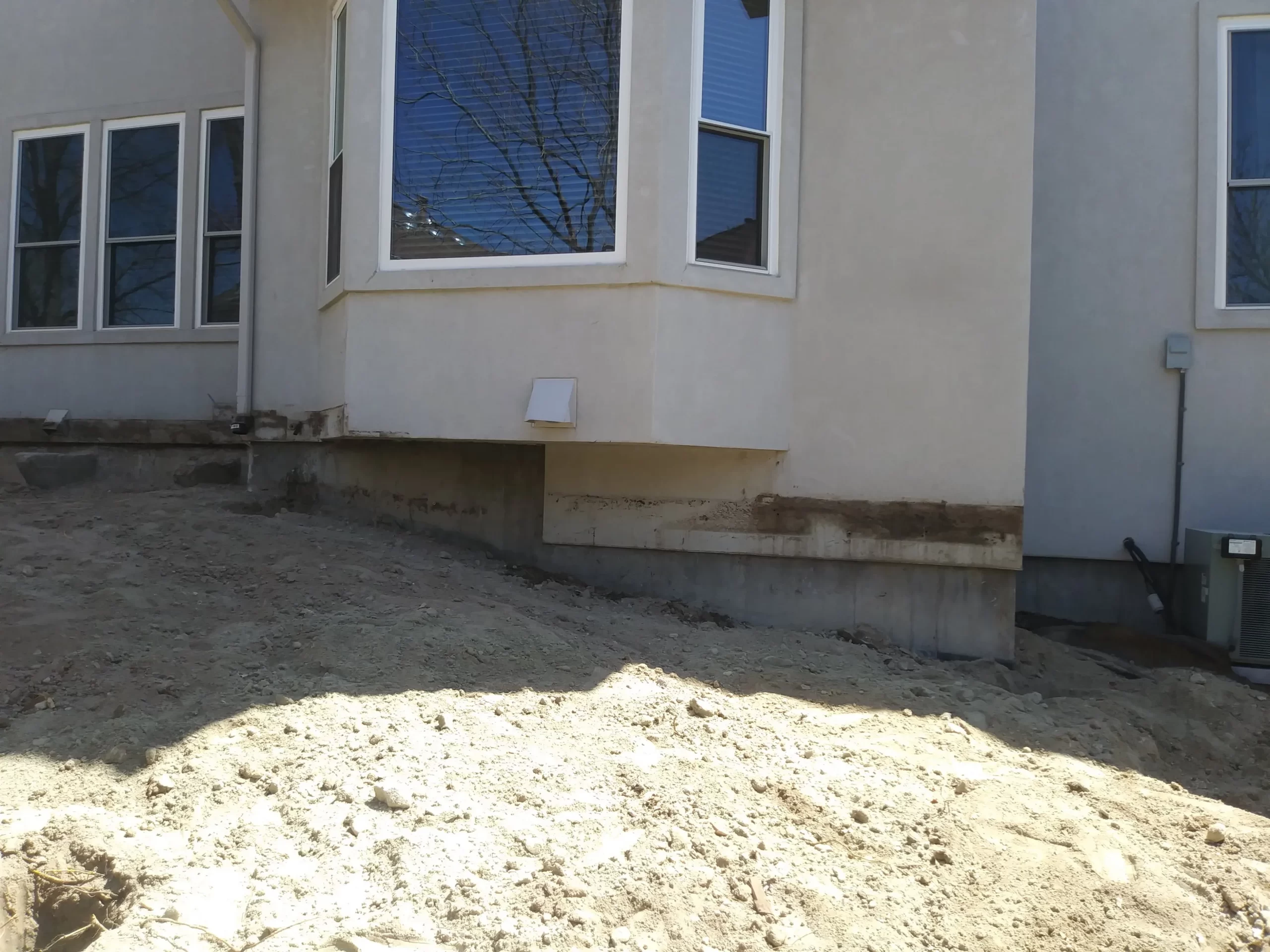 gallery (16) Residential house exterior showing bay window, beige walls, and unfinished ground at the base.