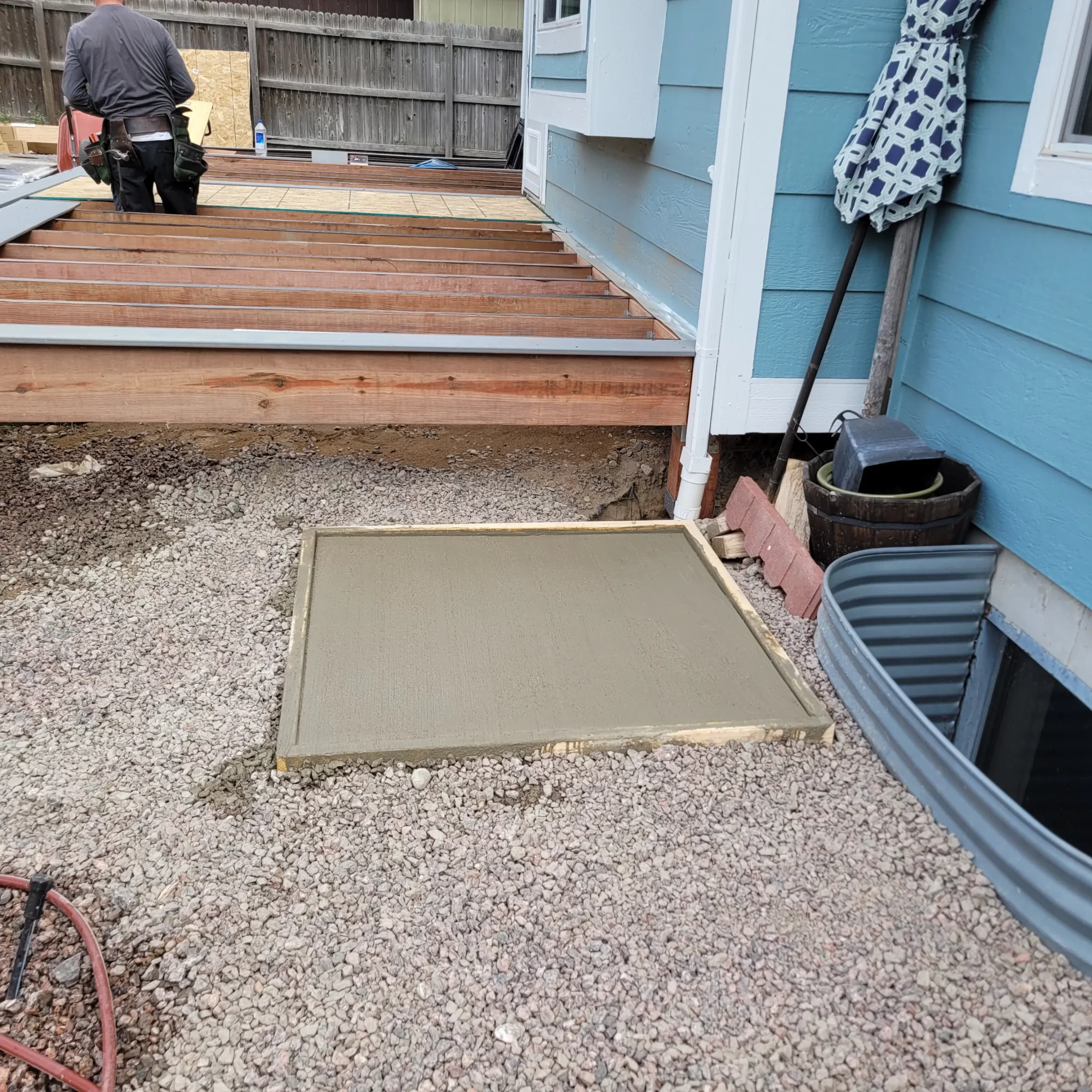 gallery (18) A freshly poured concrete slab next to a deck under construction with a person working on the wooden deck.