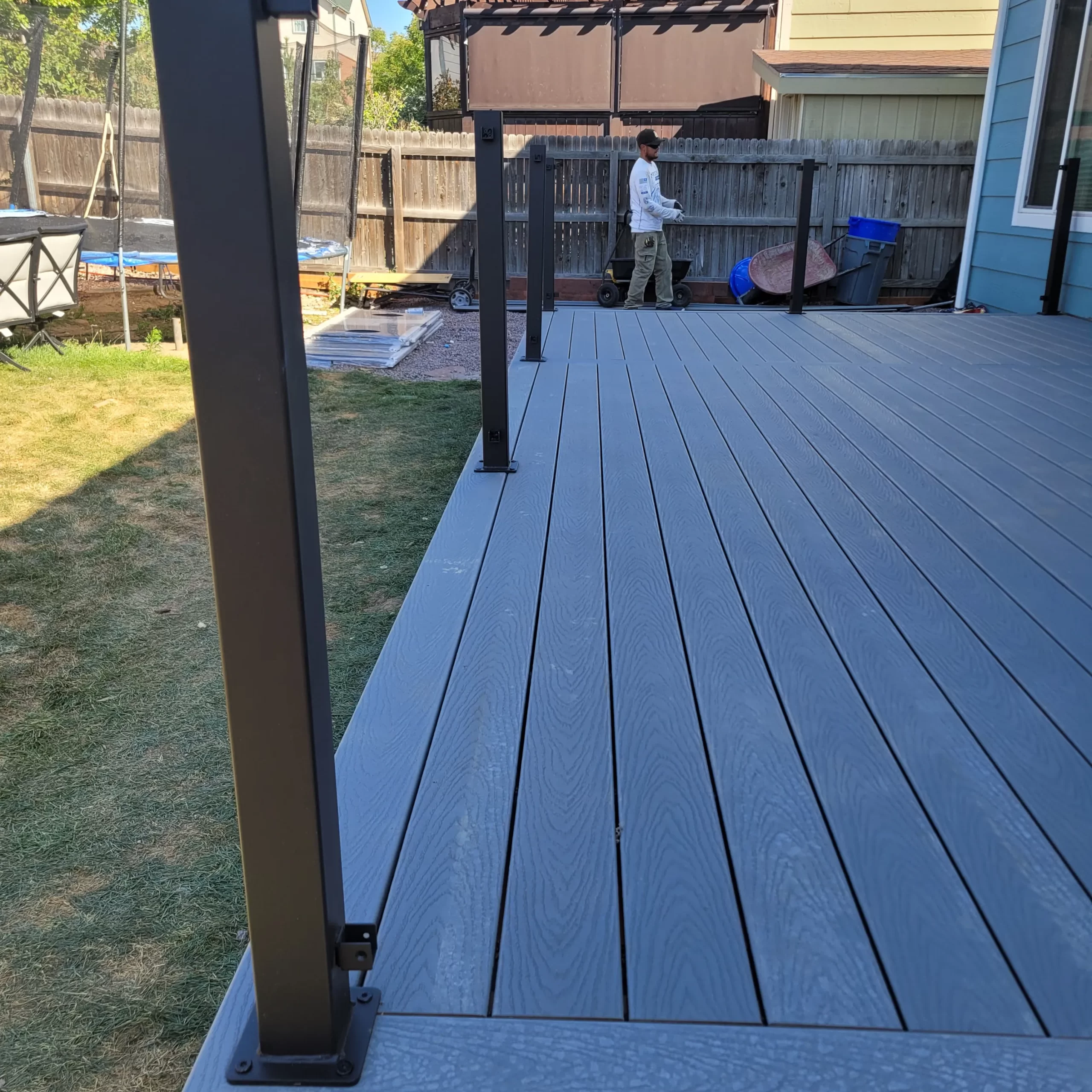 gallery (19) Gray composite deck with metal railing posts, overlooking a grassy yard and a person near a fence in the background.