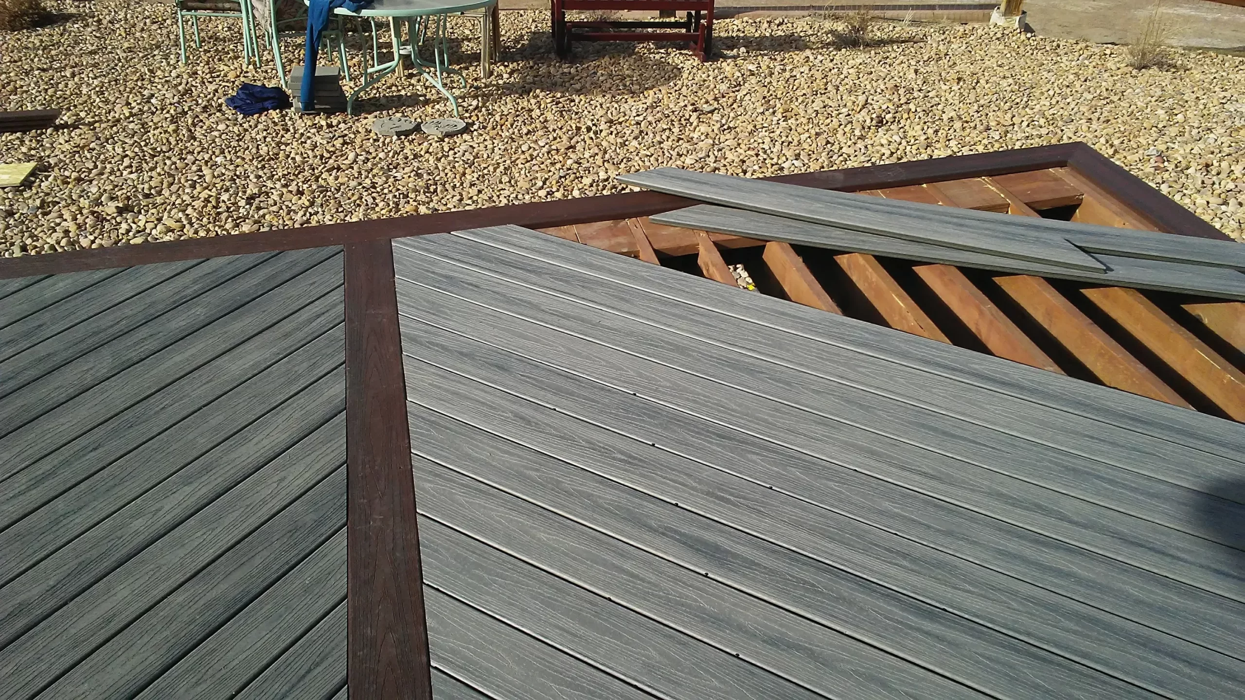 gallery (24) Broken gray composite decking with fallen boards on a brown wooden frame surrounded by gravel.