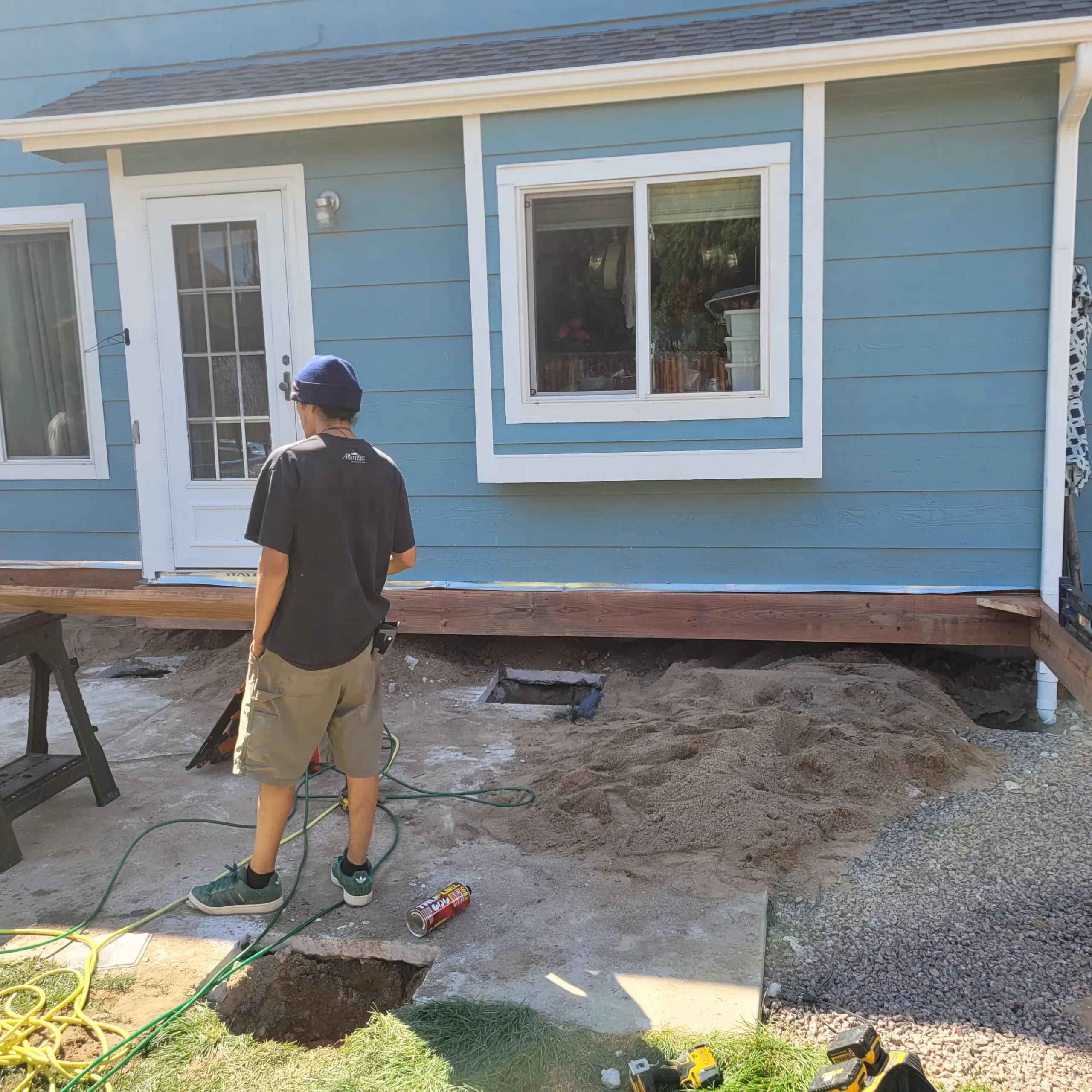 gallery (25) Person in casual attire works on a construction project outside a blue house.