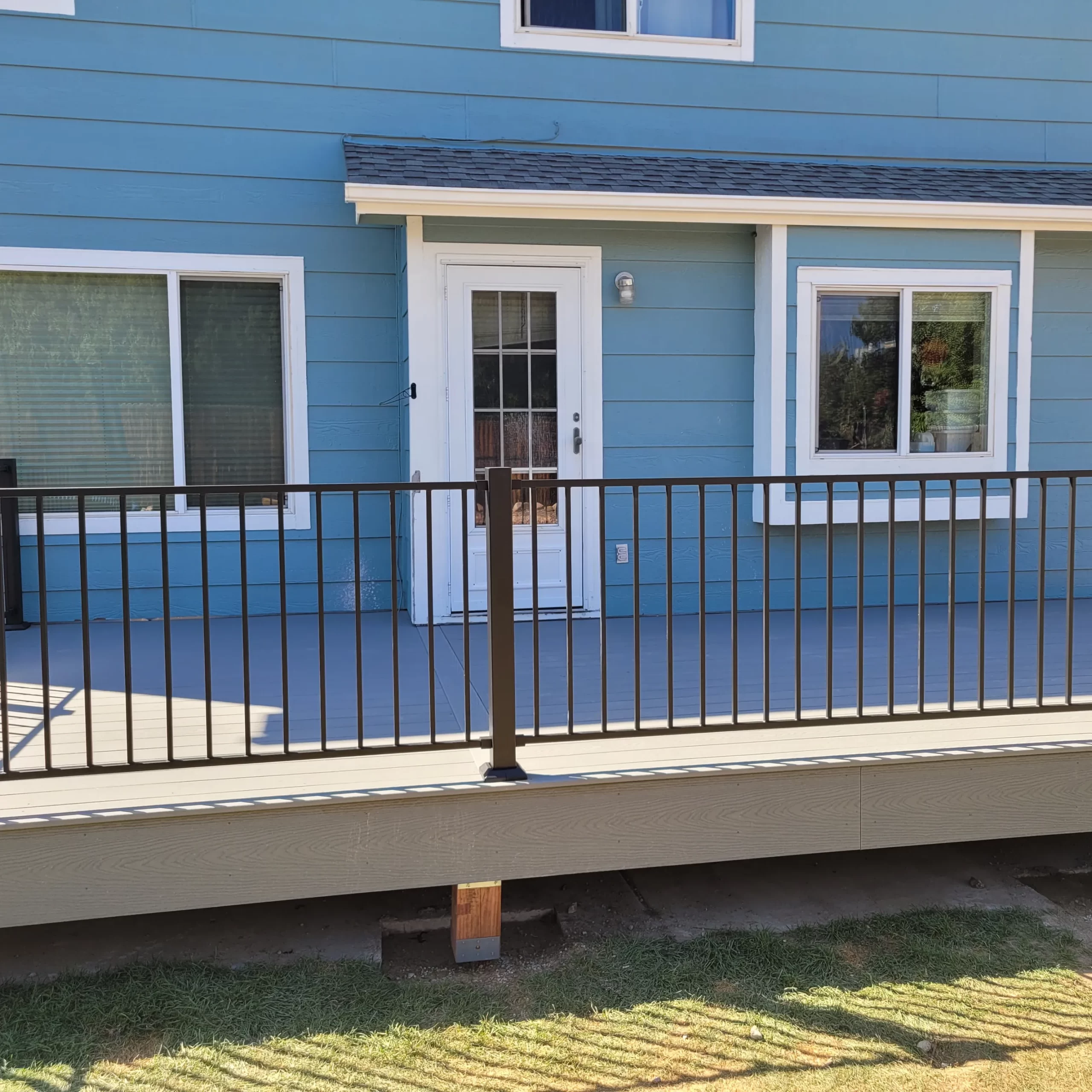 gallery (28) A blue house with white-trimmed windows and a glass door, featuring a wooden deck with black metal railing.