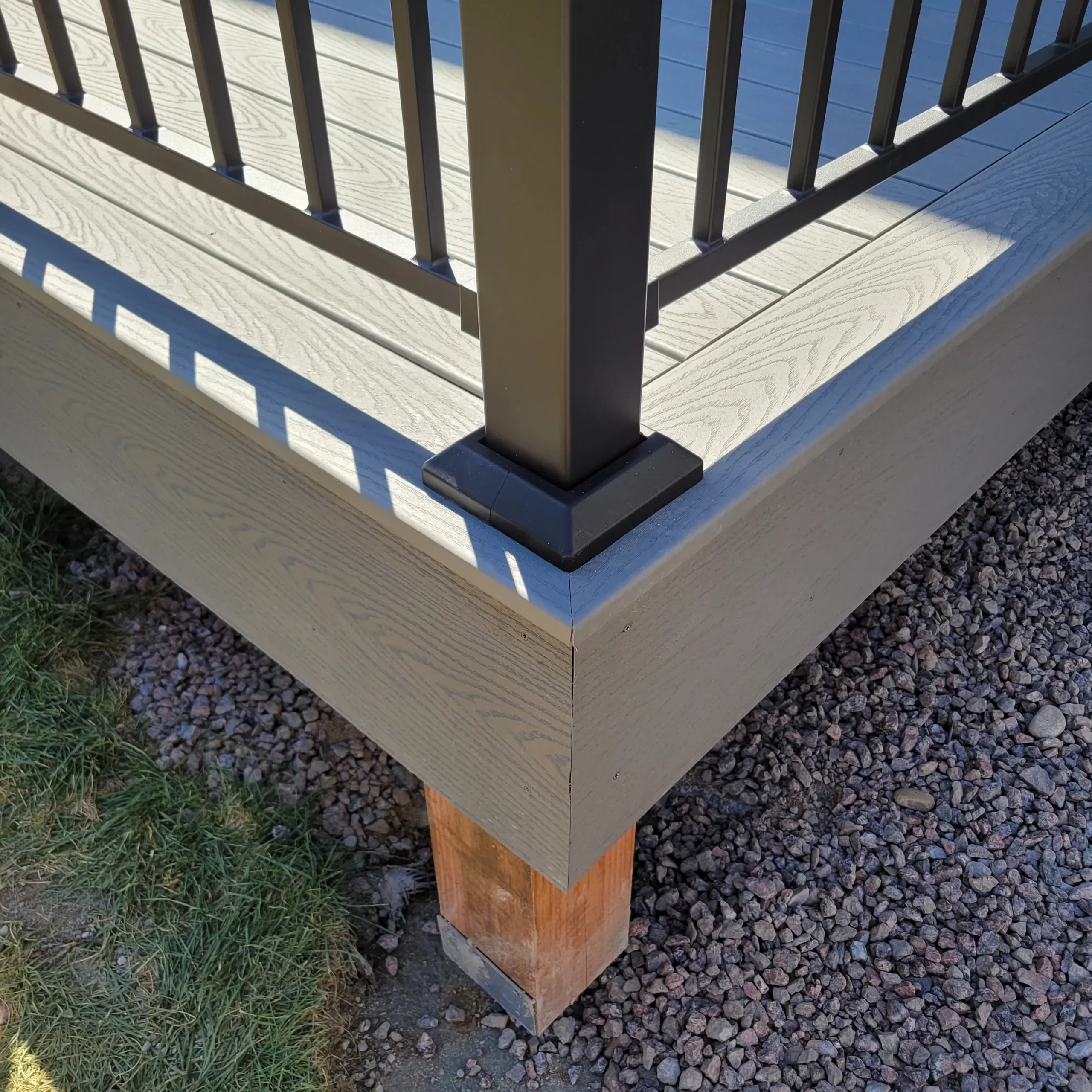gallery (29) Corner of a wooden deck with metal railing posts and gravel ground below.