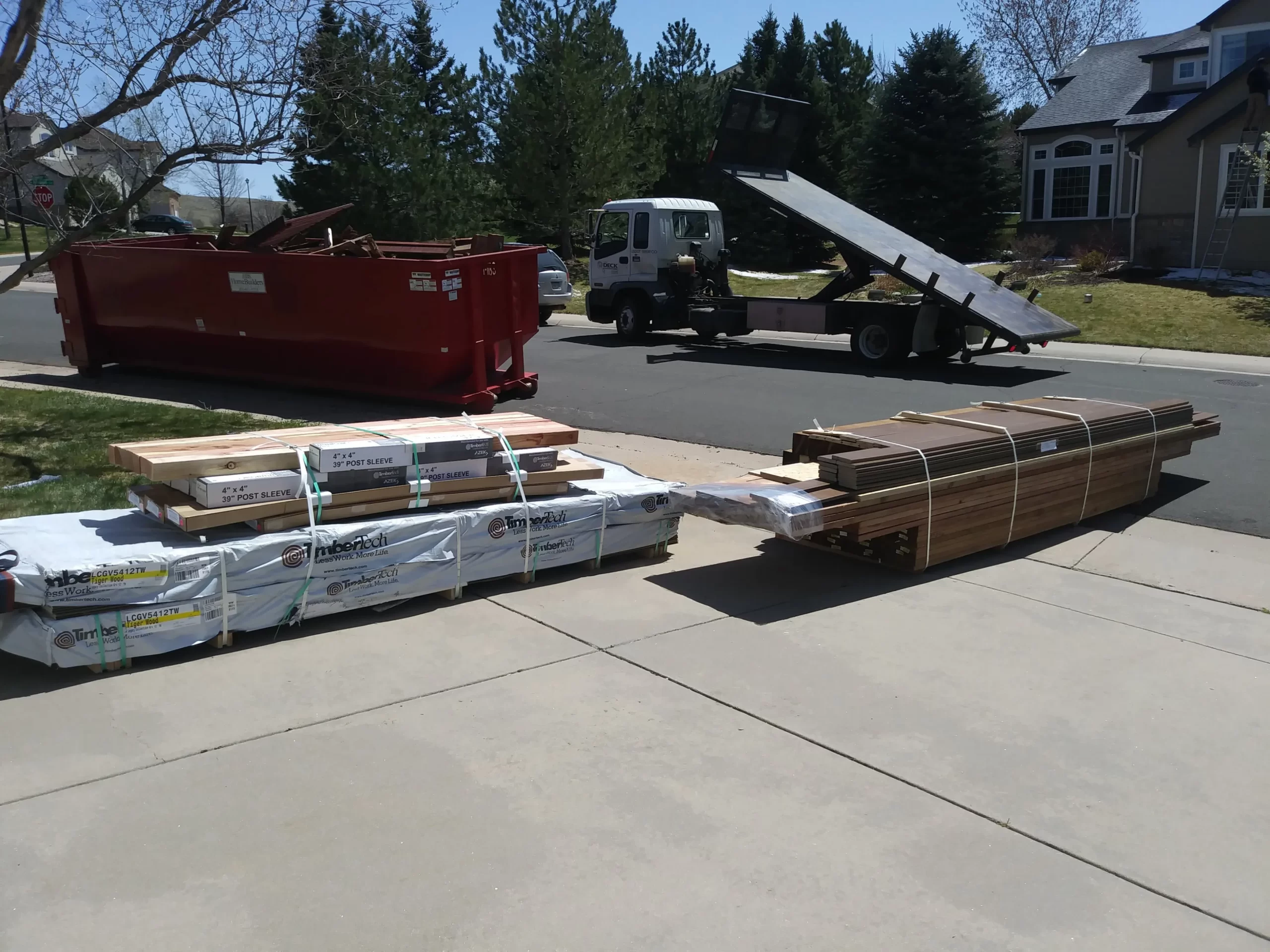 gallery (30) Construction materials on a driveway with a red dumpster and white truck nearby on a suburban street.