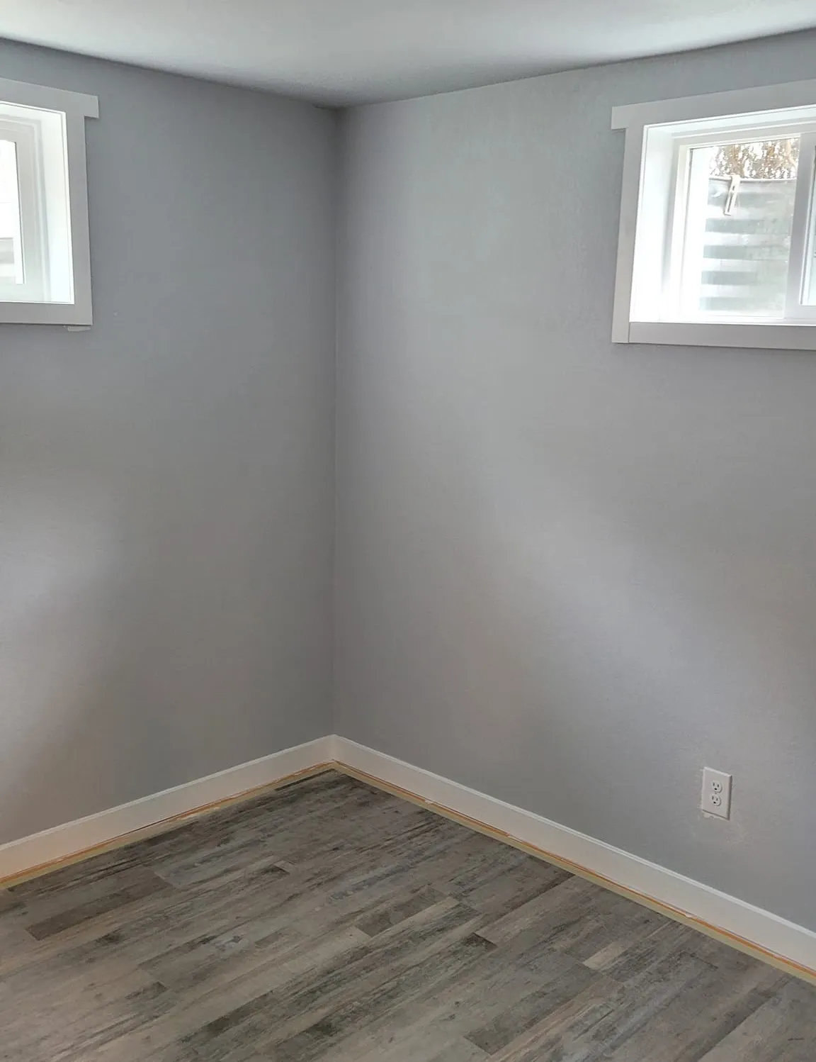 basement-finishing-1 Basement Finishing Services - Great Dane Construction: Empty room with gray walls, light wood flooring, and two small windows near the ceiling.