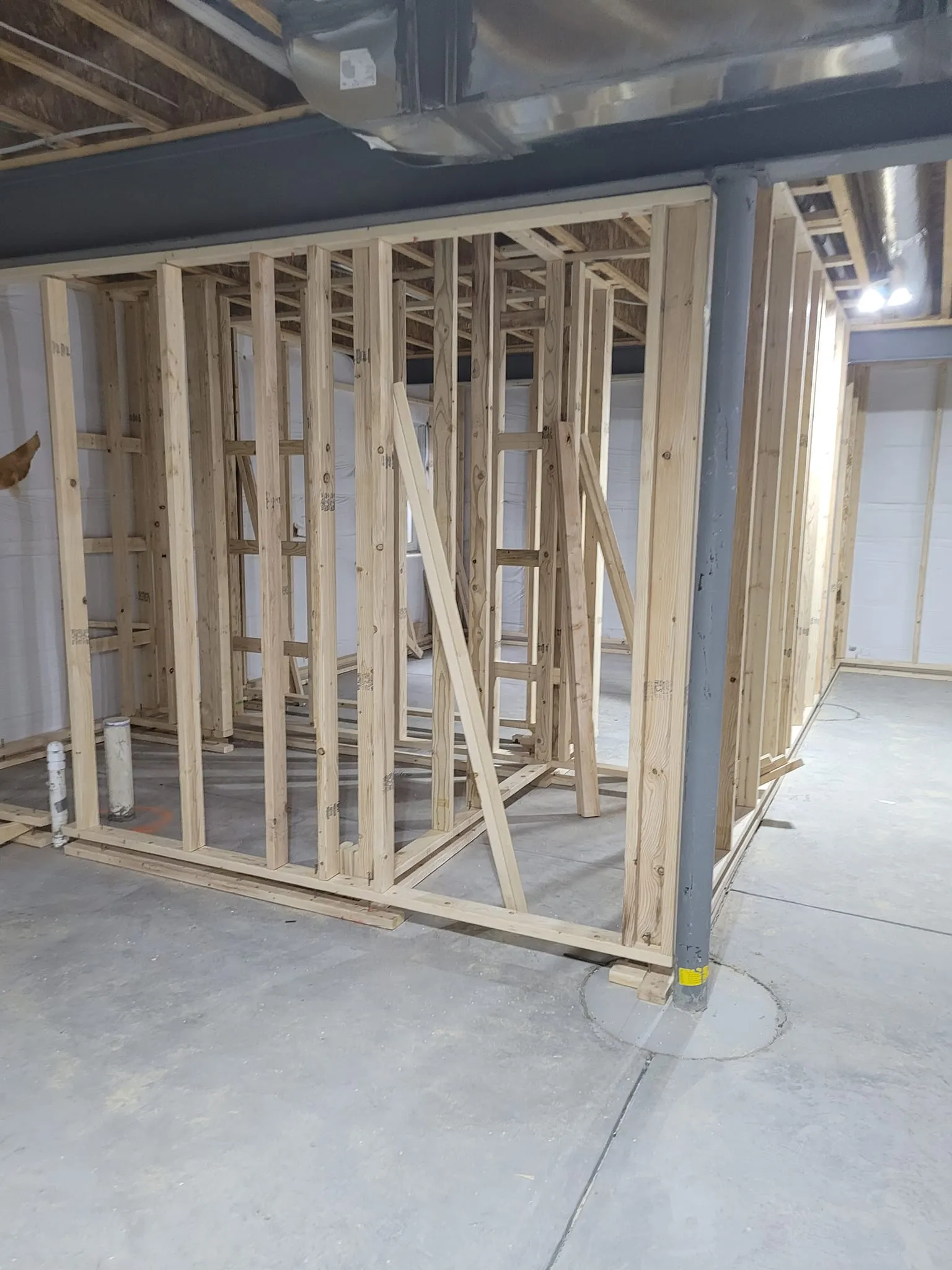 basement-framing-2 Wooden framing structure under construction in a room with cement flooring and exposed ceiling beams.
