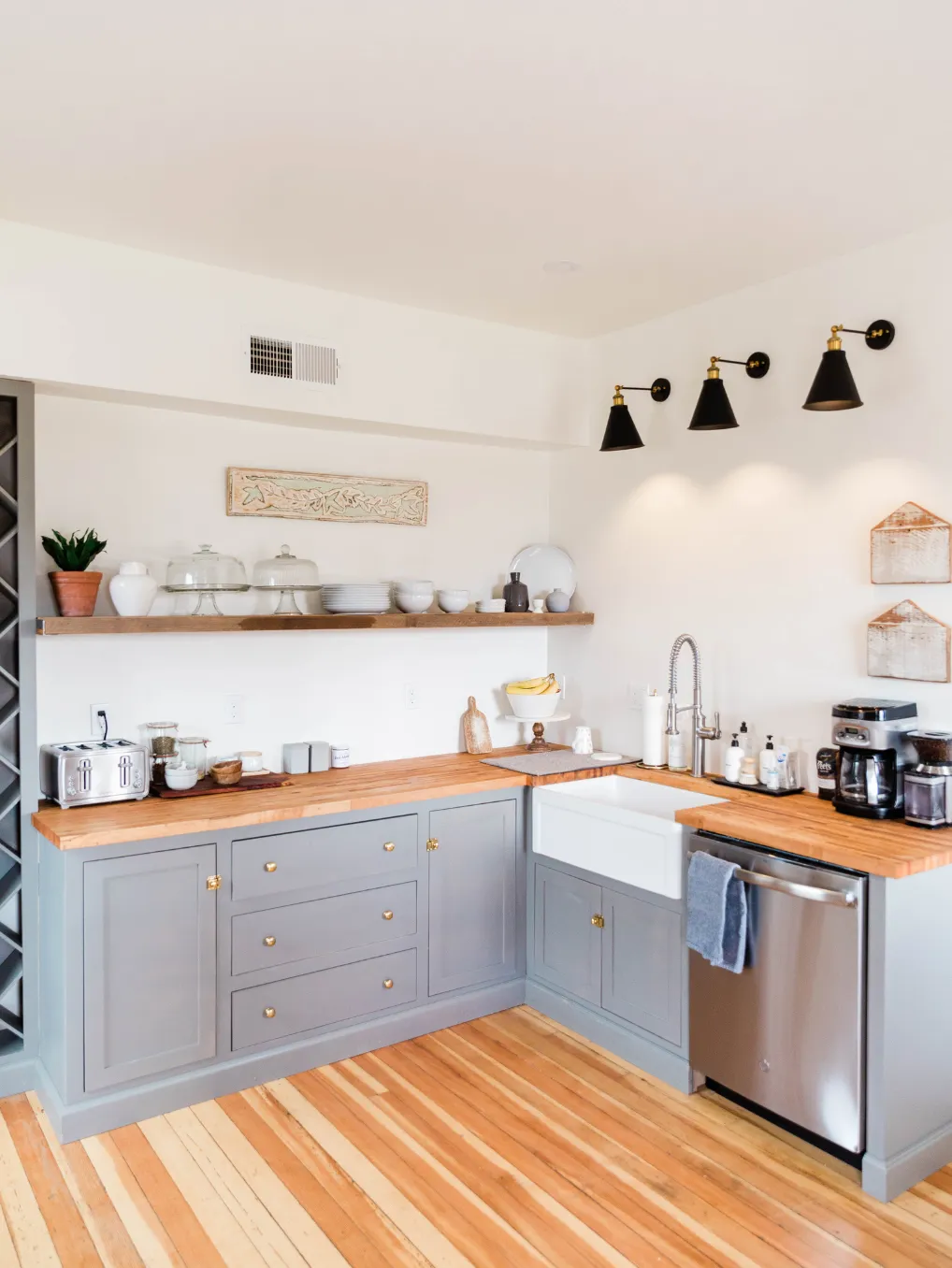 A modern kitchen with gray cabinets, open shelves, a farmhouse sink, and wooden countertops.