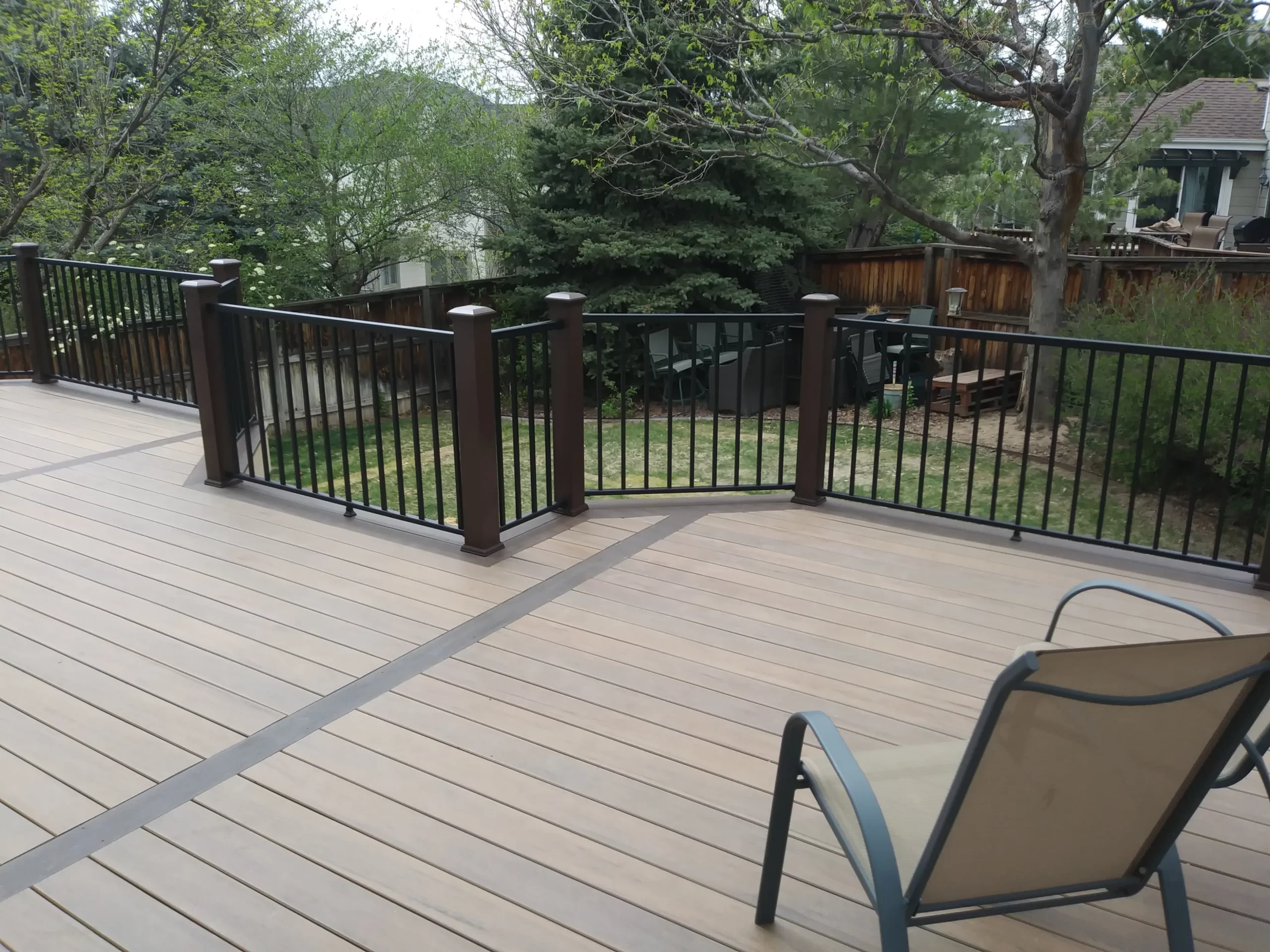 gallery-2-scaled A deck with a metal railing overlooks a backyard with trees; a single chair is on the deck.